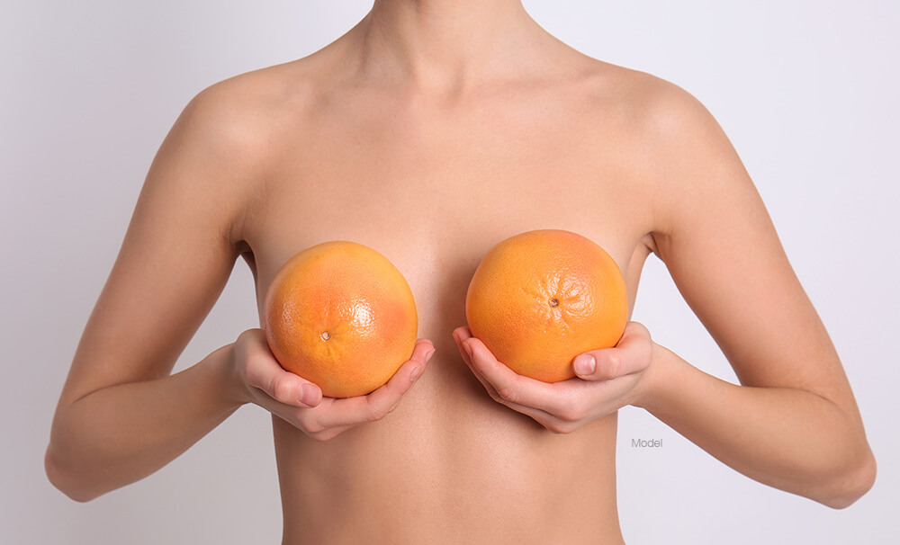 woman holds grapefruits in front of chest to resemble breasts